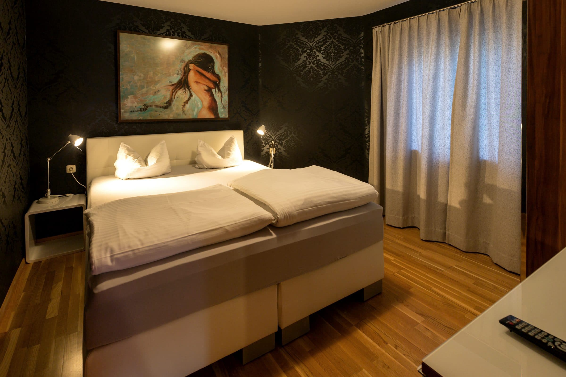 Schlafzimmer der Prachtbude mit dunkler Damasttapete, Gemälde und Boxspringbett